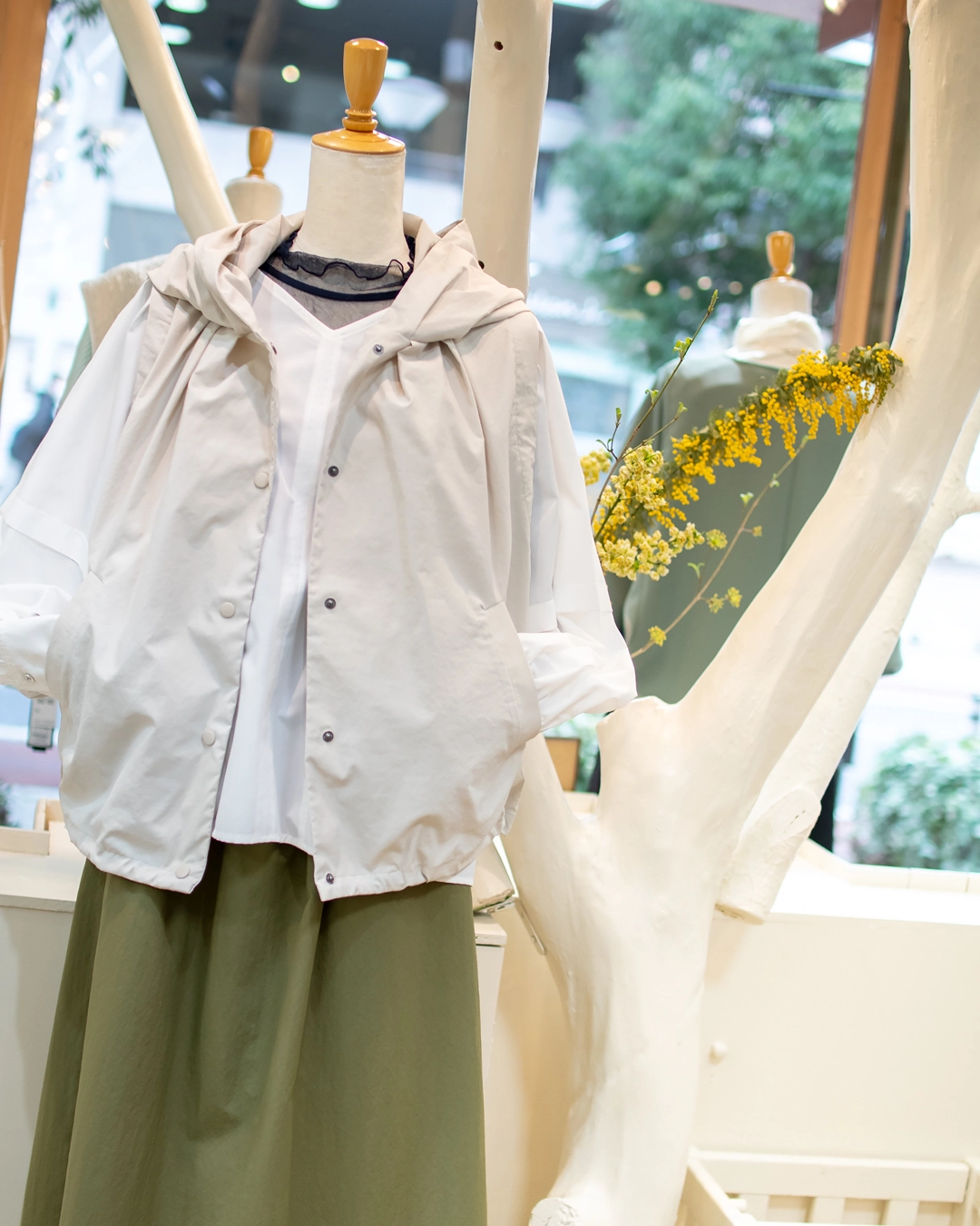 春のベストコーディネート。フーデッドベスト、白ブラウス、グリーンスカートのレイヤードスタイル。