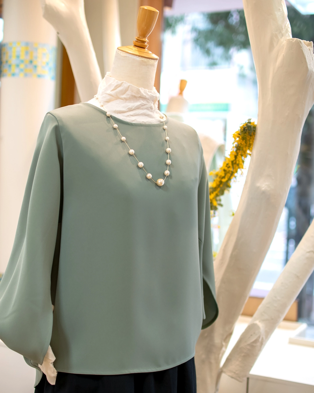 大人の春のニュアンスカラーコーデ。セージグリーンのブラウス、白のハイネック、パールネックレスの組み合わせ。