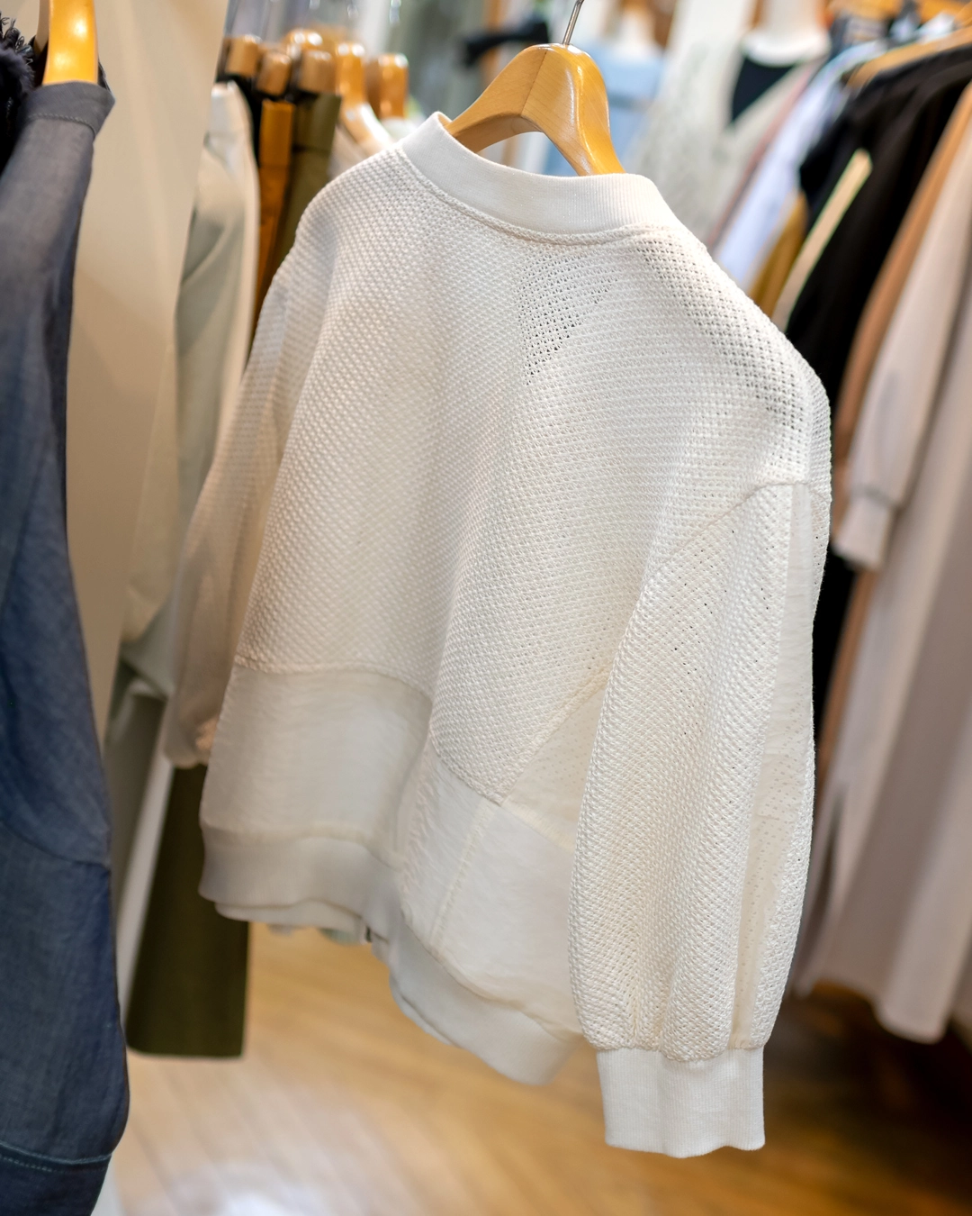 ハンガーに掛かった白のメッシュ素材で裾がシアーのブルゾン。背面のデザイン。