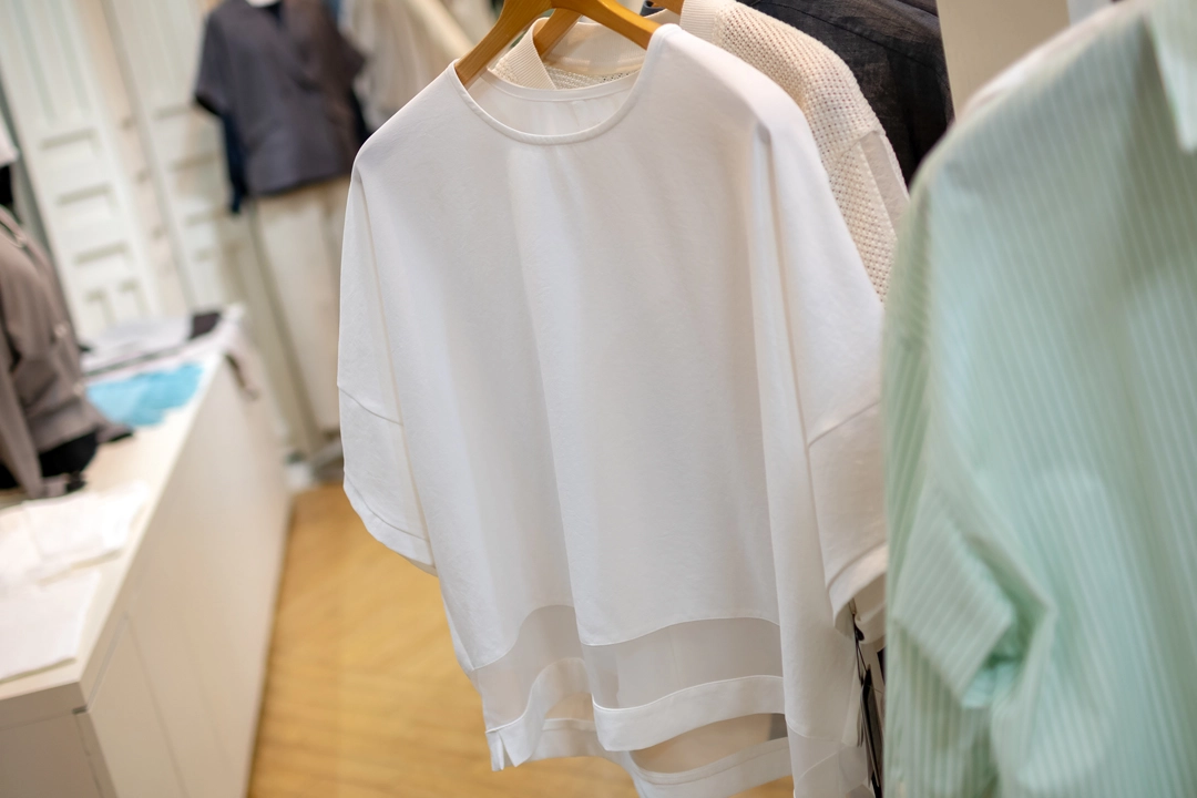 ハンガーに掛かった白の半袖プルオーバー。裾の部分がシアーな透け感のある素材に切り替えられているデザイン