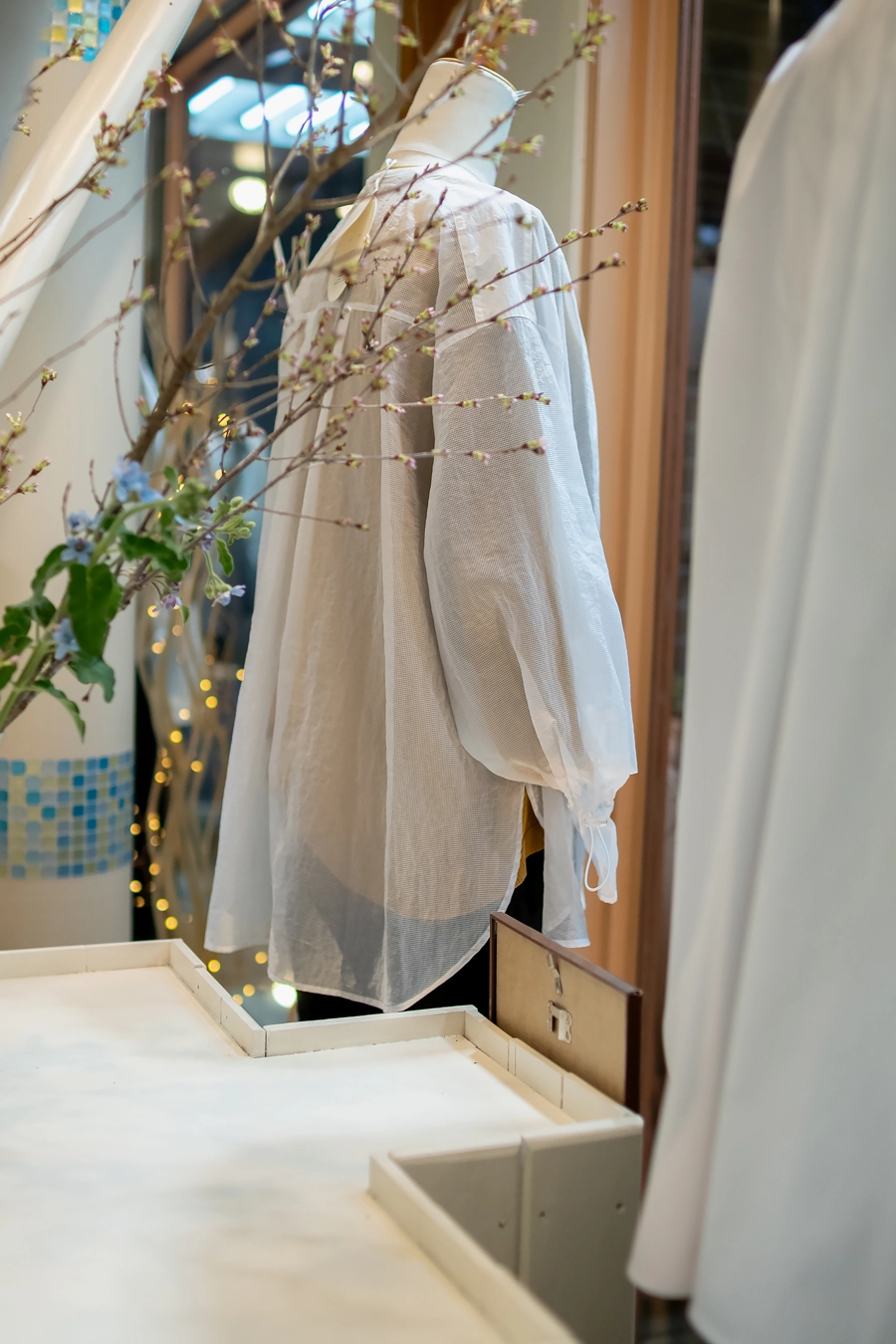 トルソーに展示された、切り替えがある白のシアーメッシュバンドカラーシャツ。