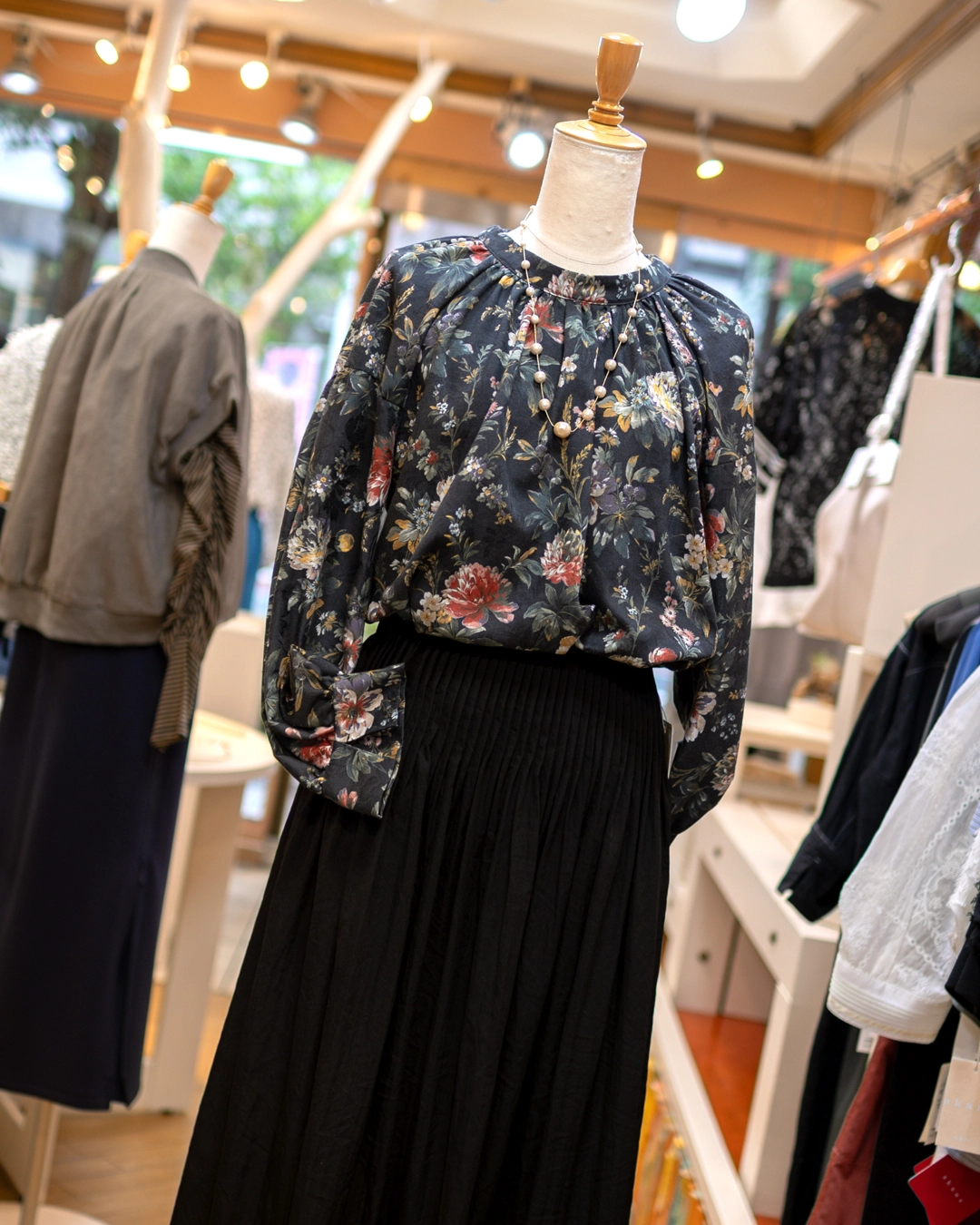 シックな黒地花柄の長袖ブラウスと黒のプリーツスカートにパールネックレスを合わせた秋コーデ