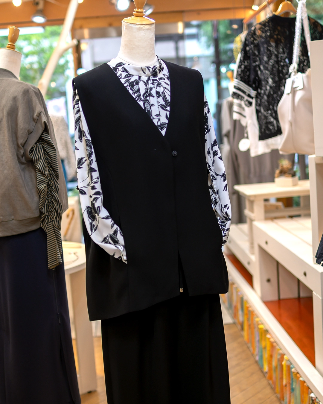 黒のシンプルなロングジレにモノトーンの花柄ブラウスを合わせた秋のレディースコーディネート