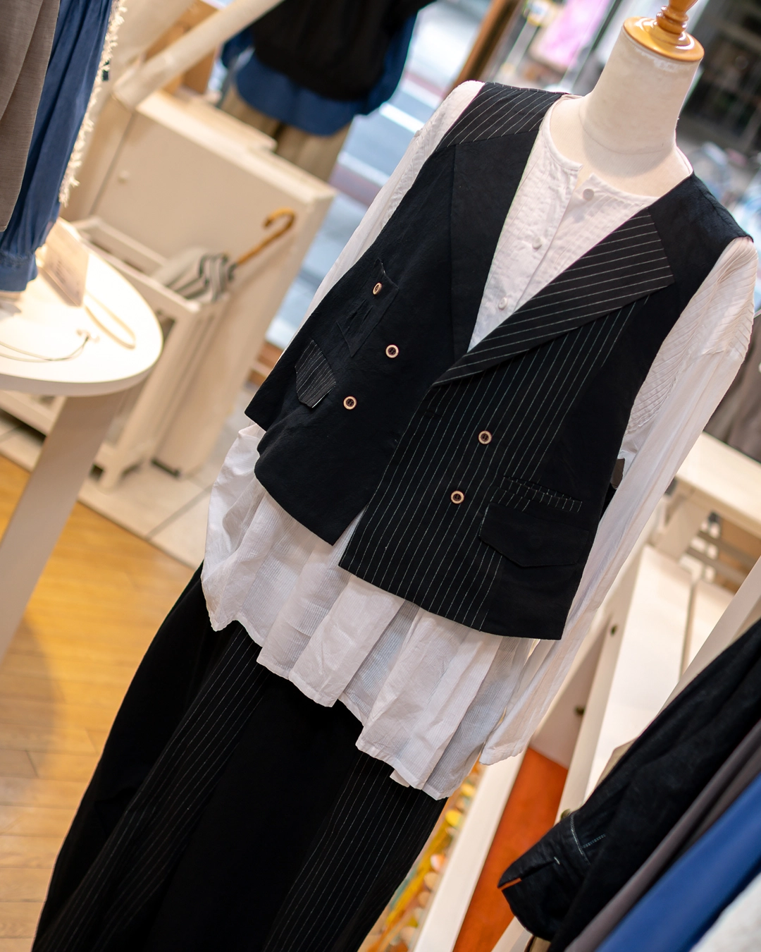黒のストライプ柄ジレとワイドパンツのセットアップに白いブラウスを重ねた秋のレディースコーディネート