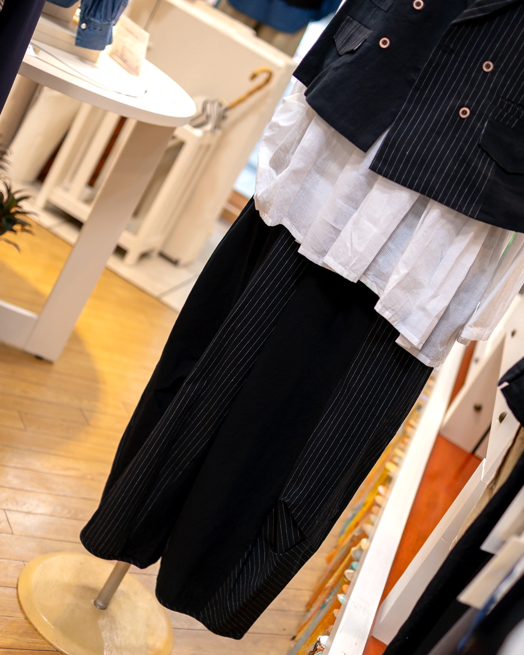 黒のストライプ柄ジレとワイドパンツのセットアップに白いブラウスを重ねた秋のレディースコーディネート